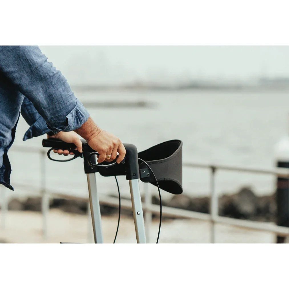 Close-up of person holding black walker handles near waterfront with blurred background
