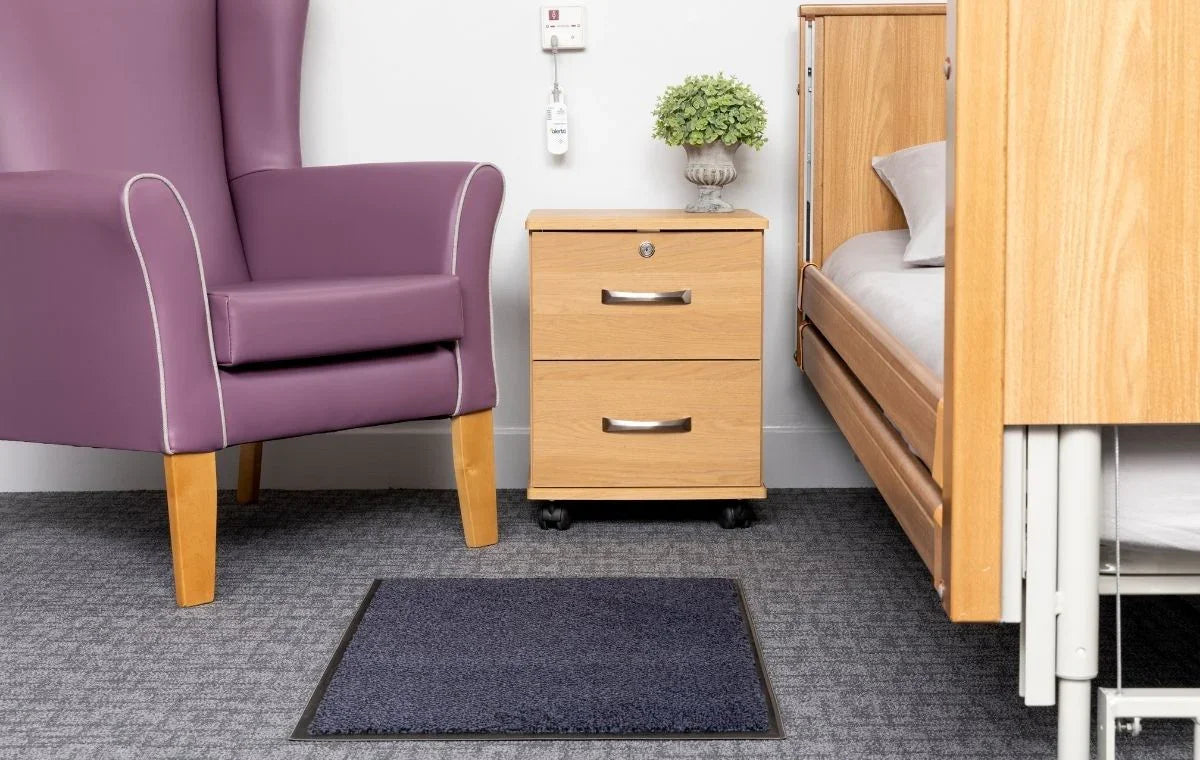 Wireless nurse call sensor mat installed near hospital bed and purple armchair in patient room